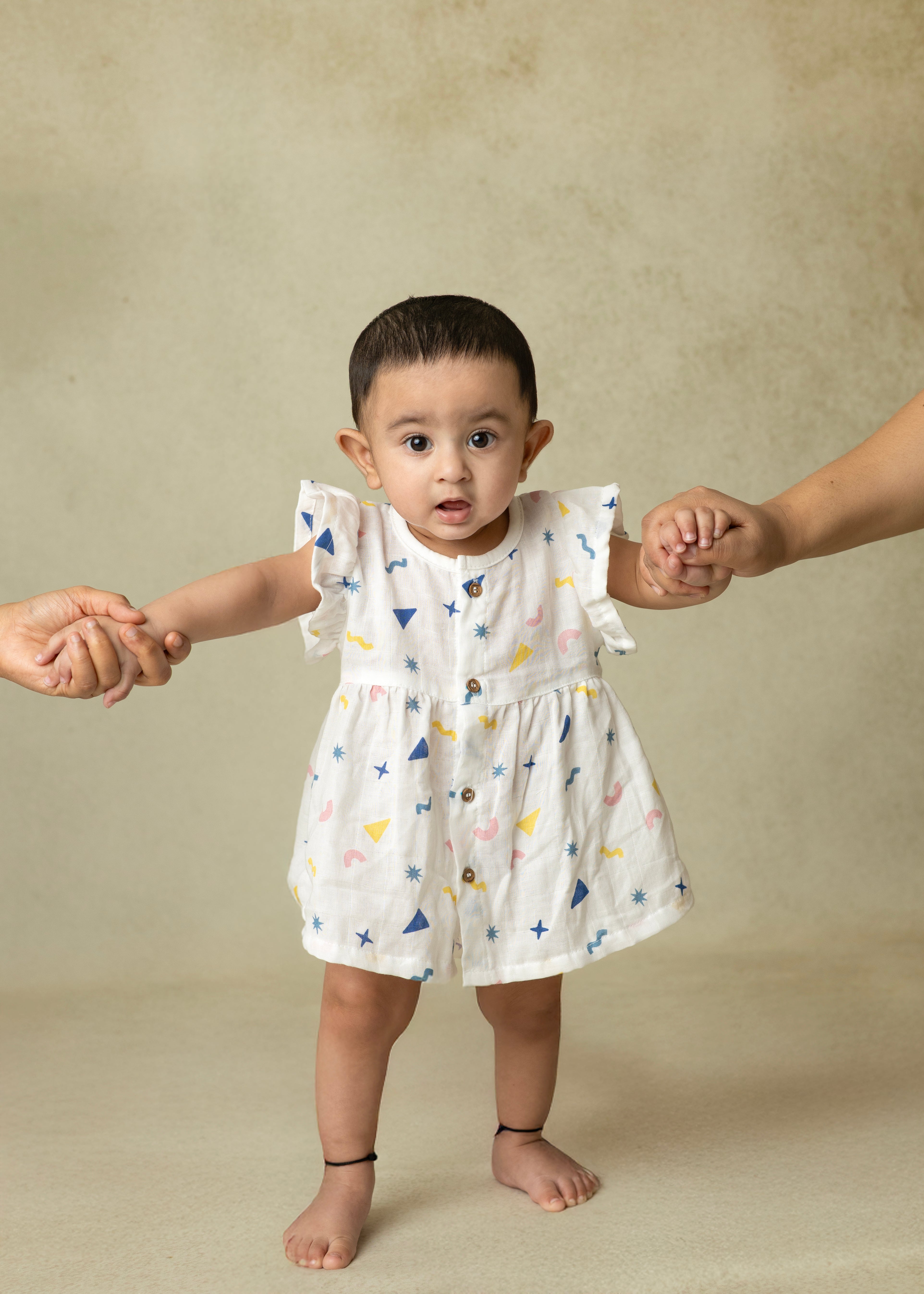 A toddler in a white ruffle sleeve frock with colorful animal prints, featuring wooden buttons and flared fit.