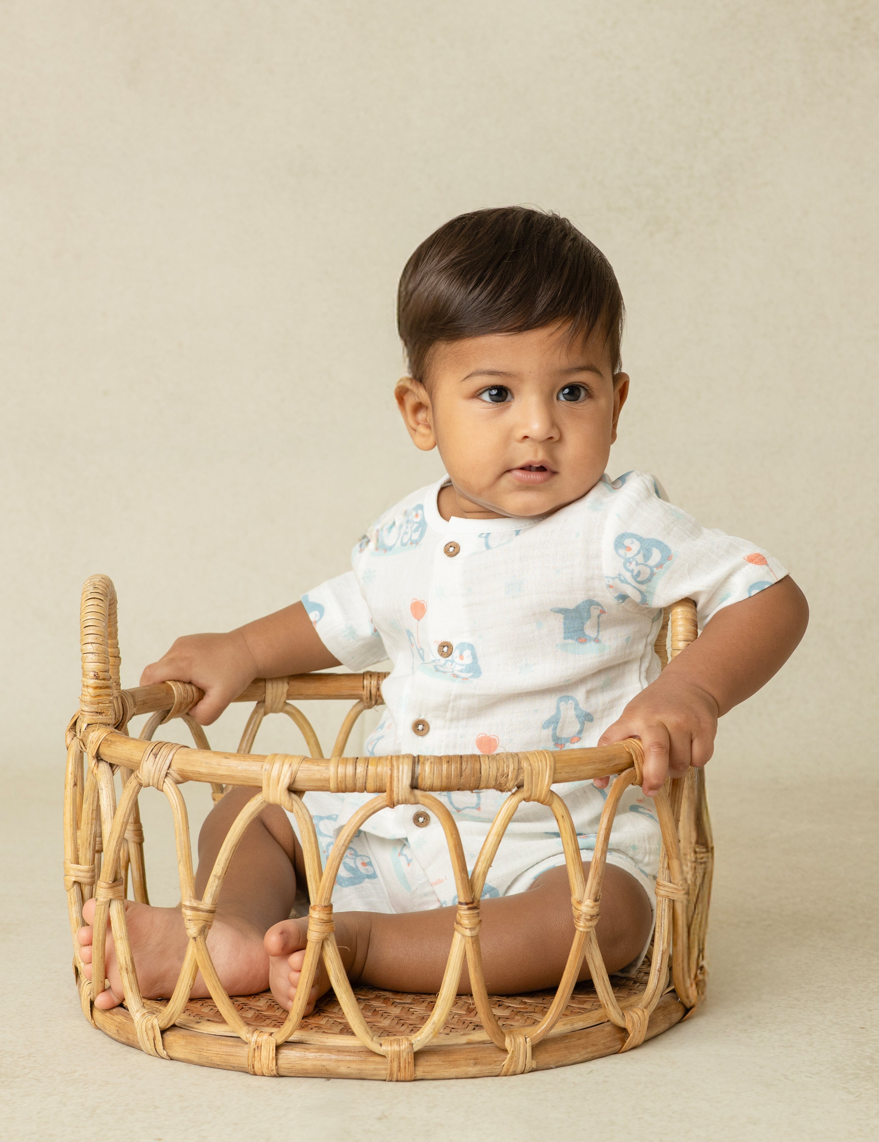 Baby sitting inside a wicker basket against a beige background