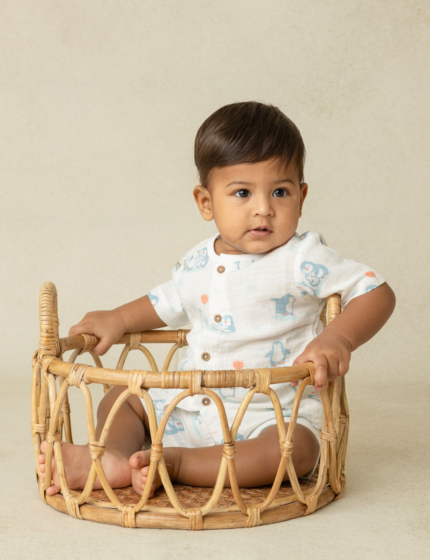 Baby sitting inside a wicker basket against a beige background