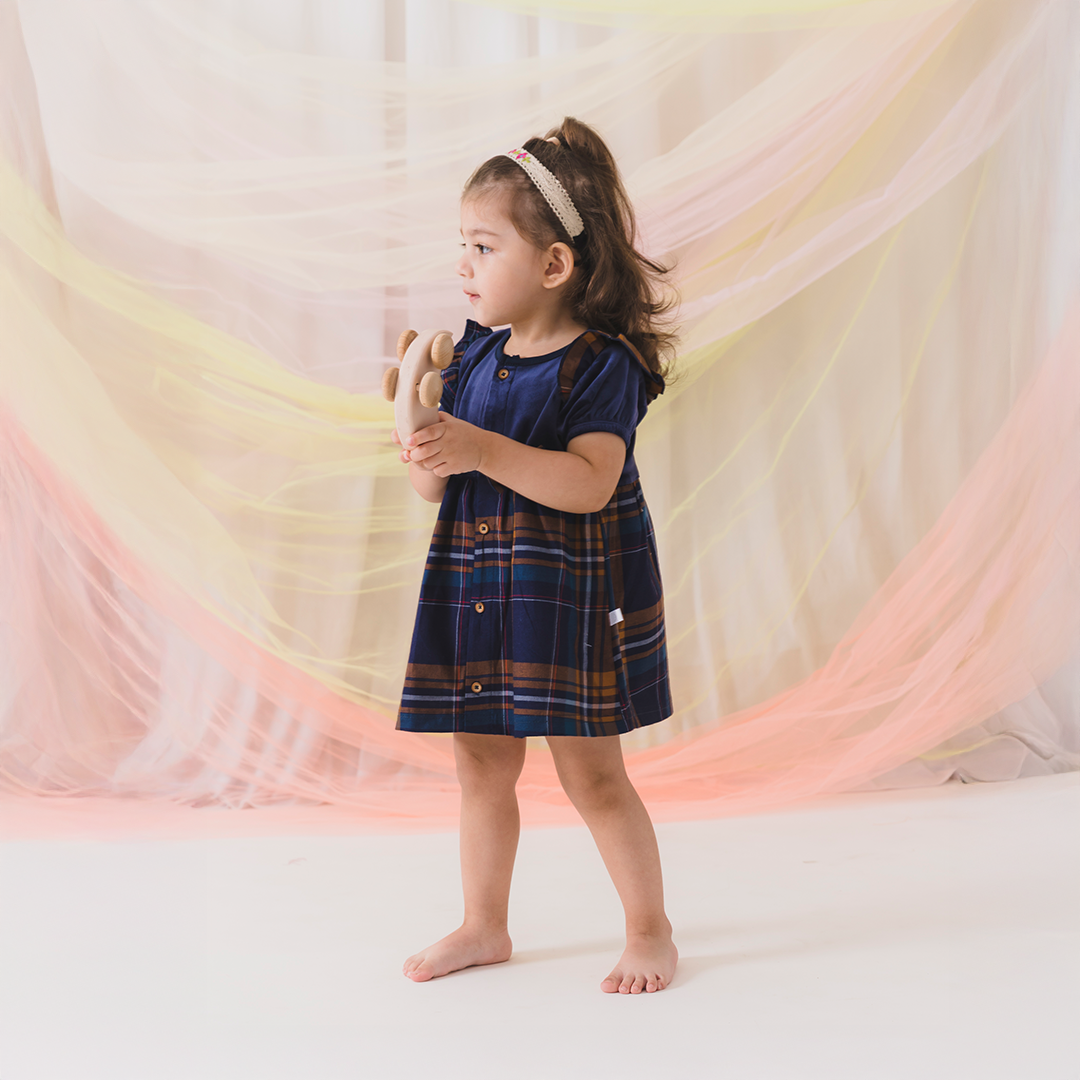 Young girl in a plaid dress holding a teddy bear against a soft, multicolored background