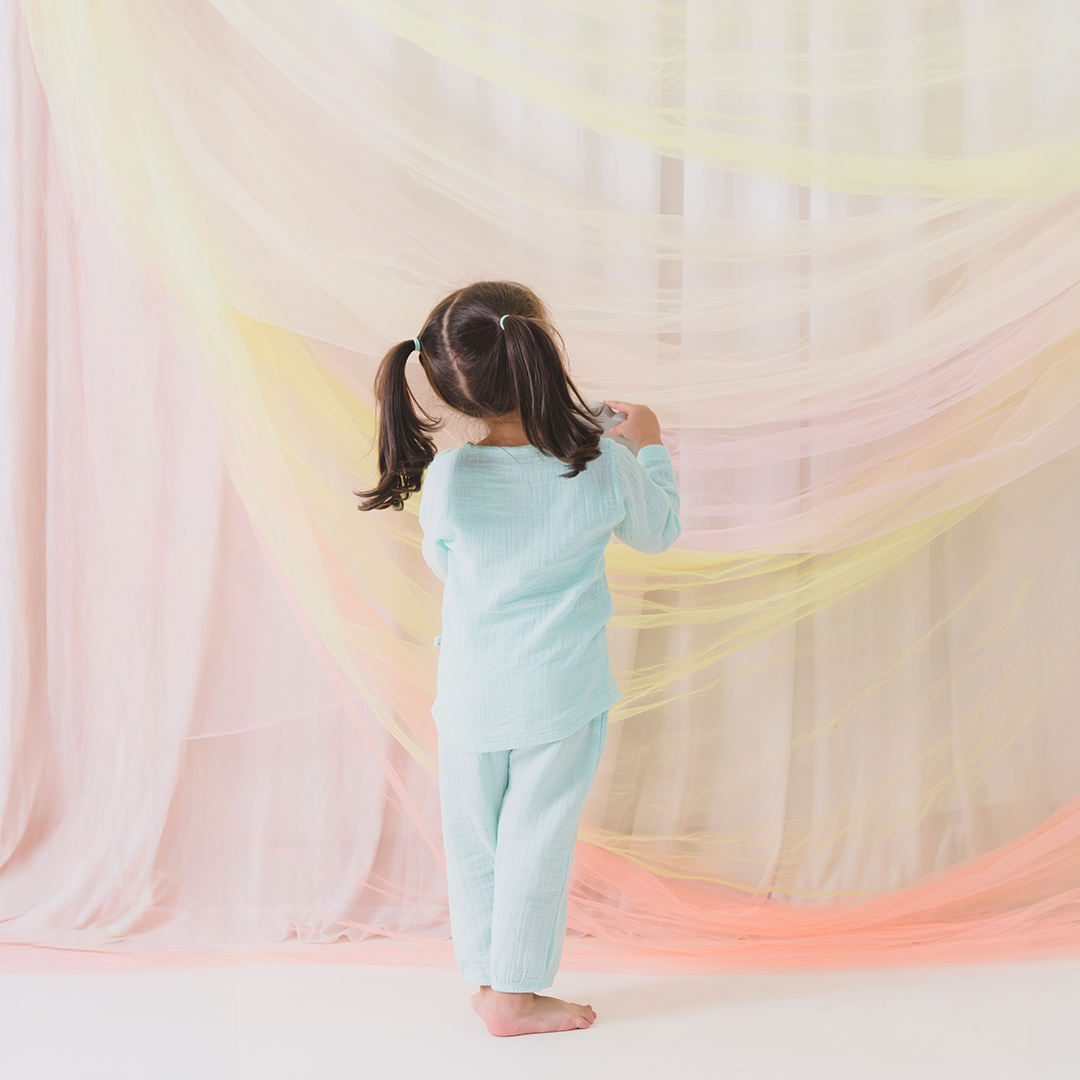 Child in light blue outfit standing in front of colorful fabric