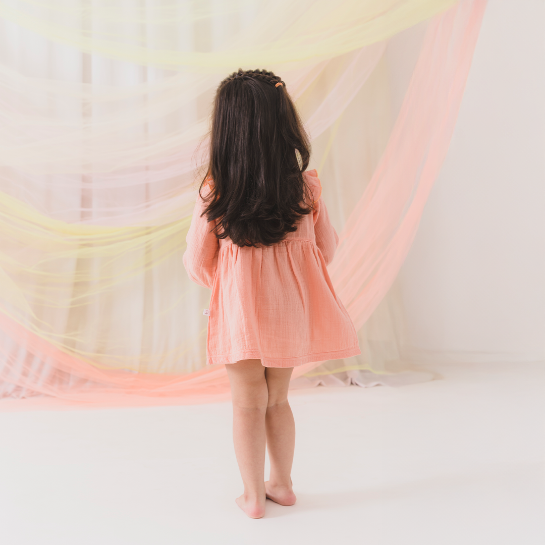 Child in a pink dress holding a colorful scarf against a white background