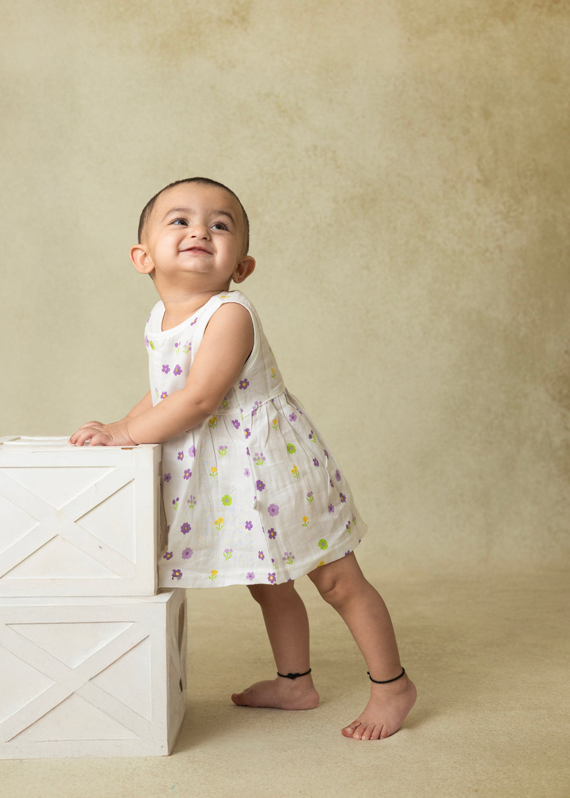 Child in a white dress with floral patterns standing on a beige background
