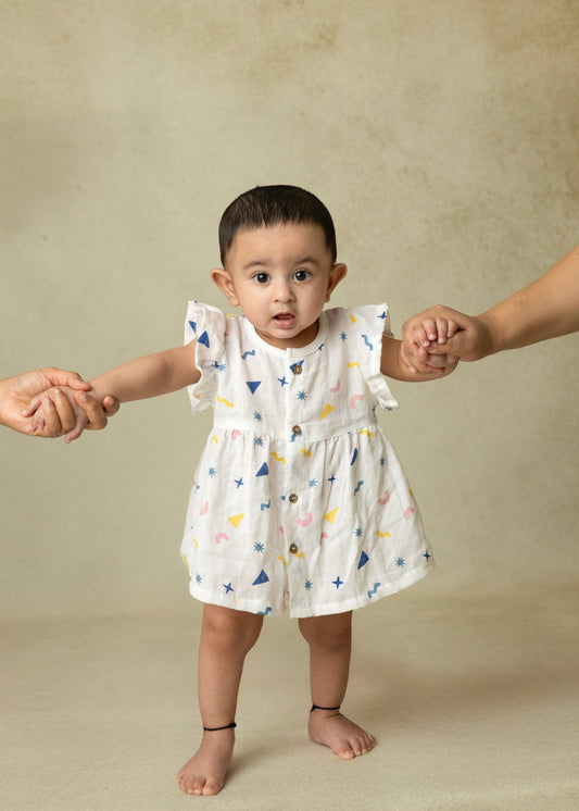 A toddler in a white ruffle sleeve frock with colorful animal prints, featuring wooden buttons and flared fit.