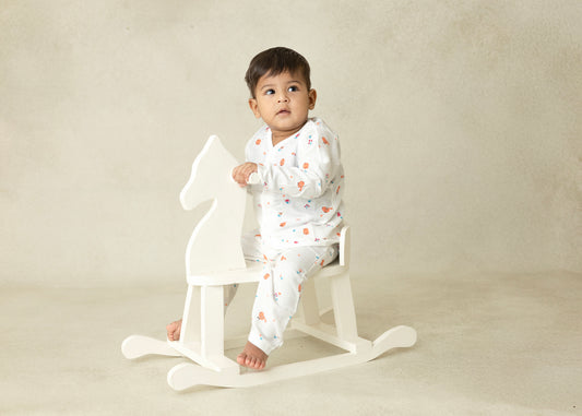 Baby sitting on a white rocking horse against a beige background