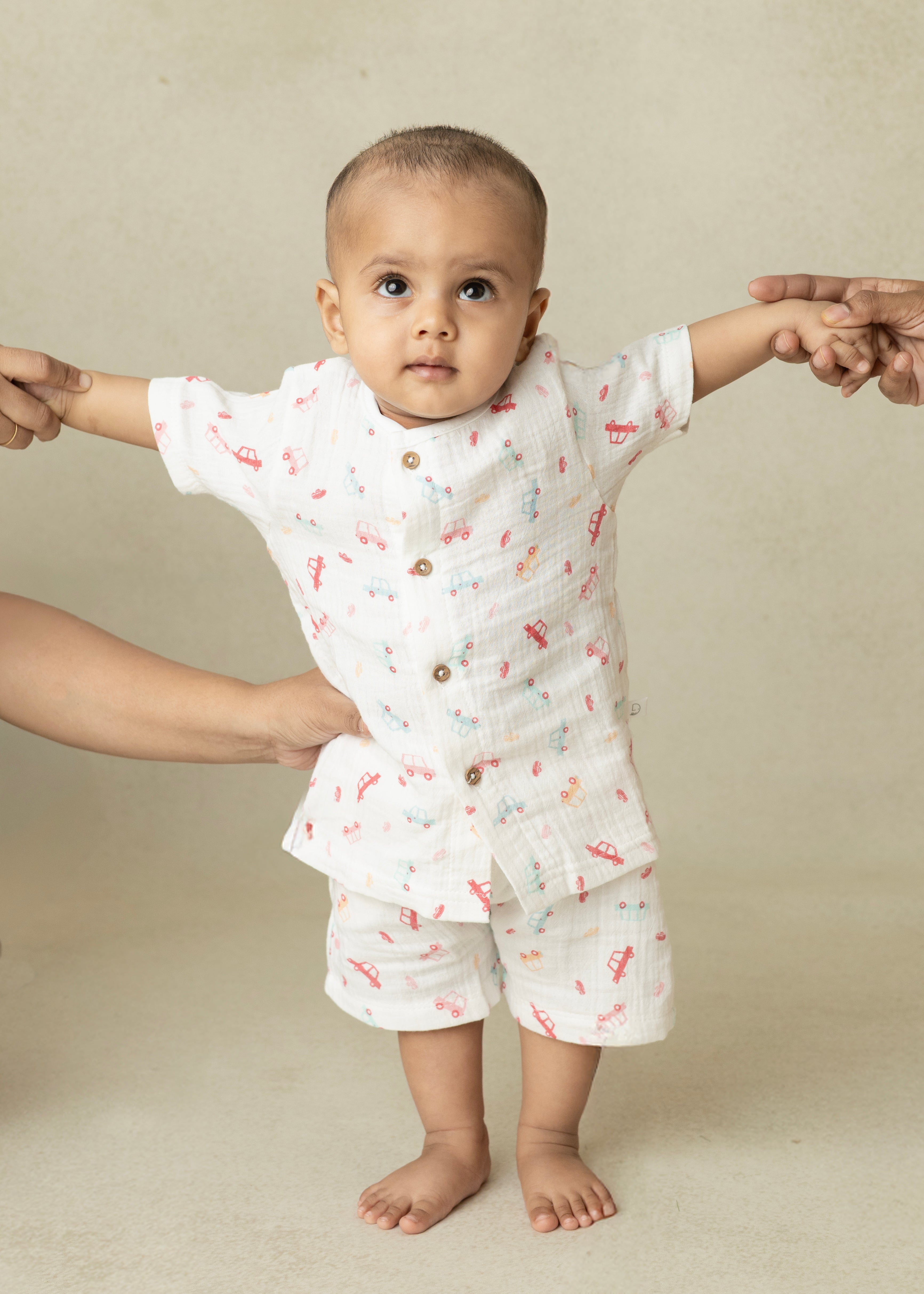 Baby in a white outfit with red patterns standing on a beige background