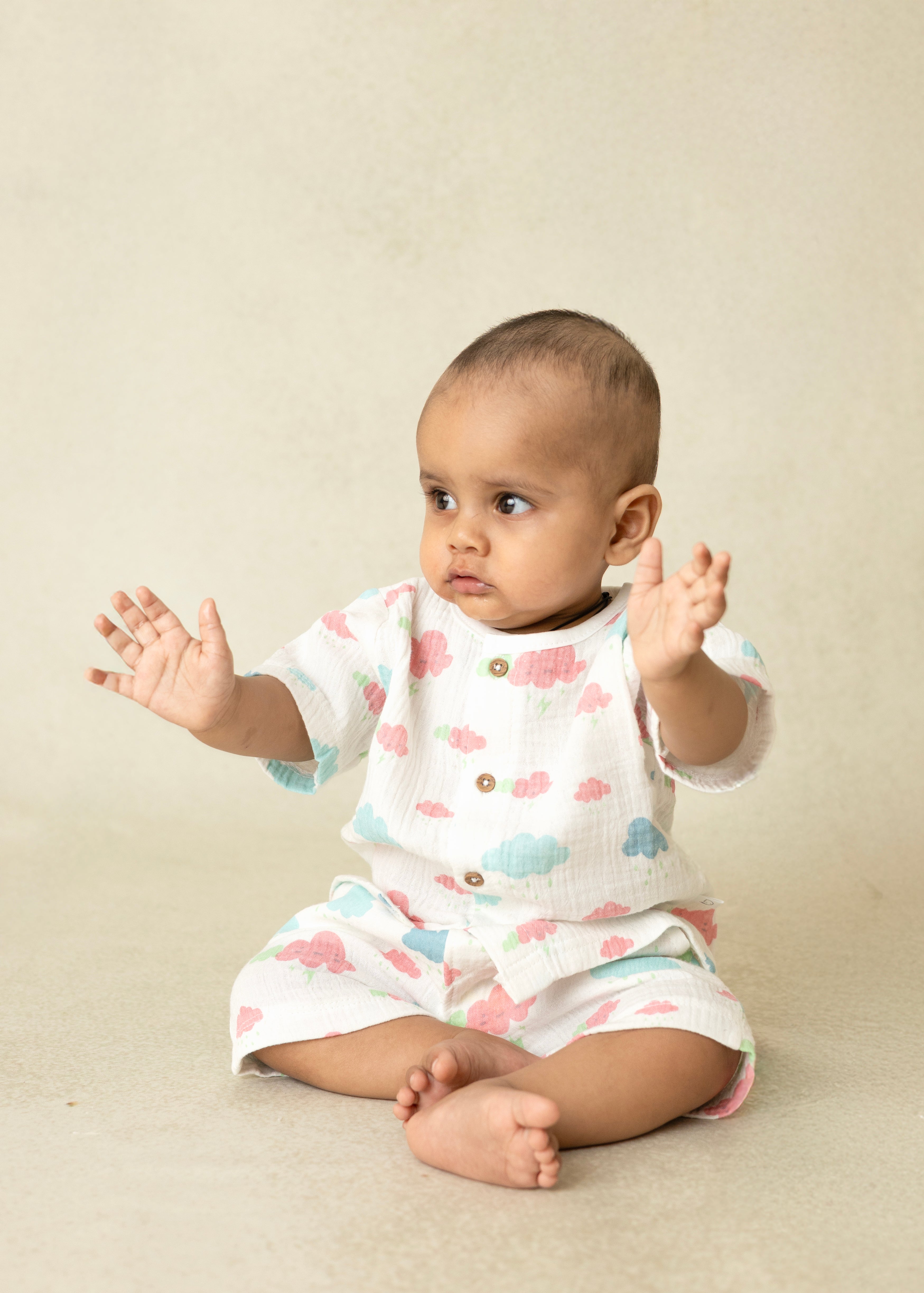 Baby wearing a white onesie with colorful cloud patterns on a beige background
