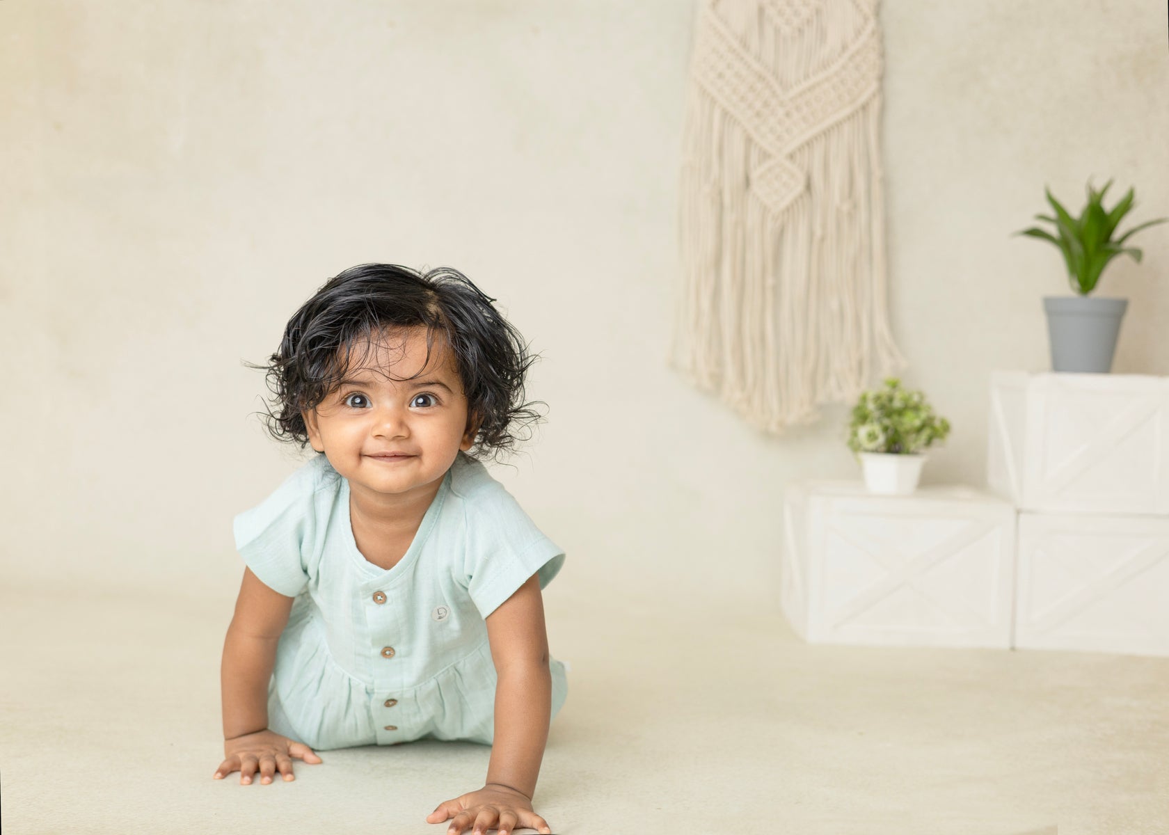 Baby in a light blue outfit sitting on a beige floor with a neutral background