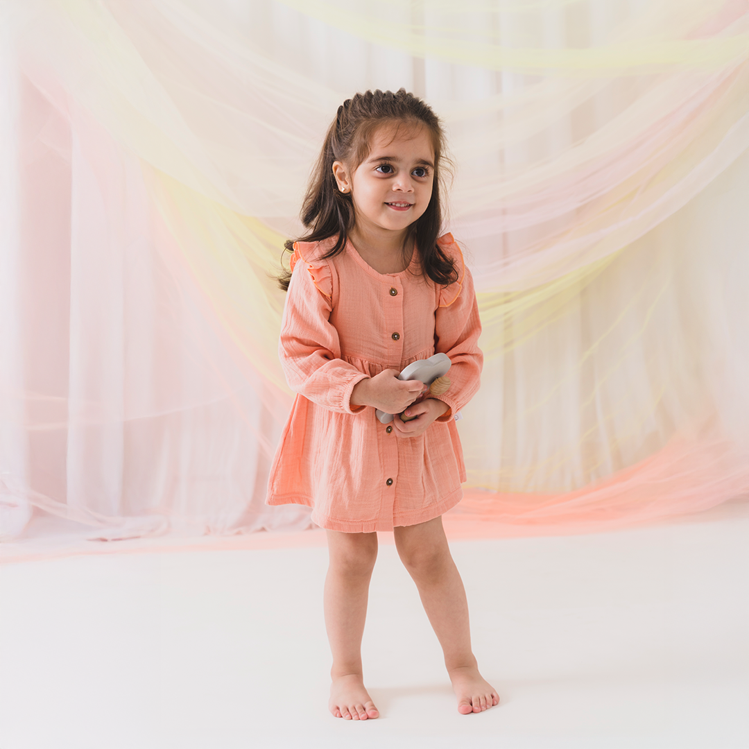 Young girl in a peach dress standing against a soft, multicolored background