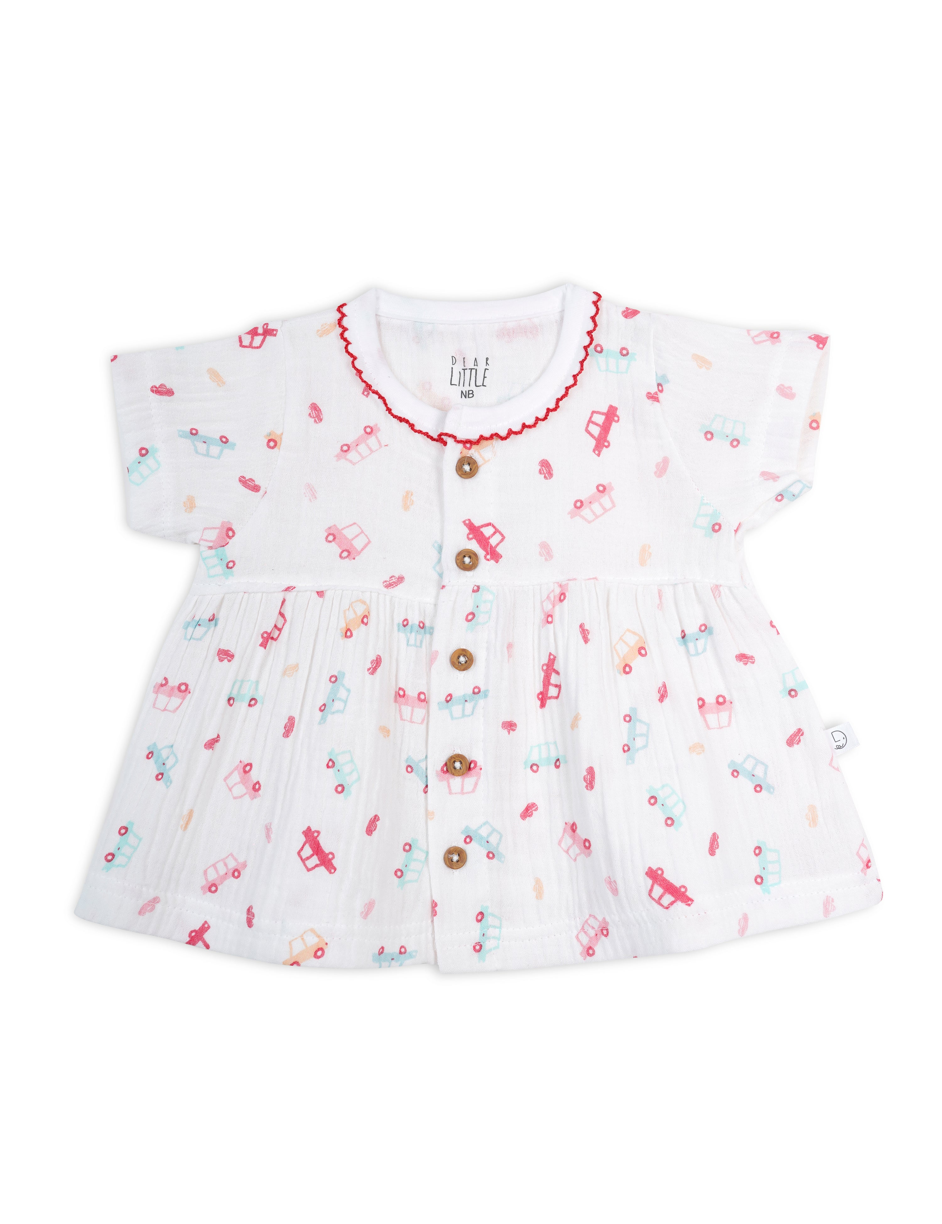 A white muslin baby frock with red wheels print and decorative trim, featuring short sleeves and buttons down the front.