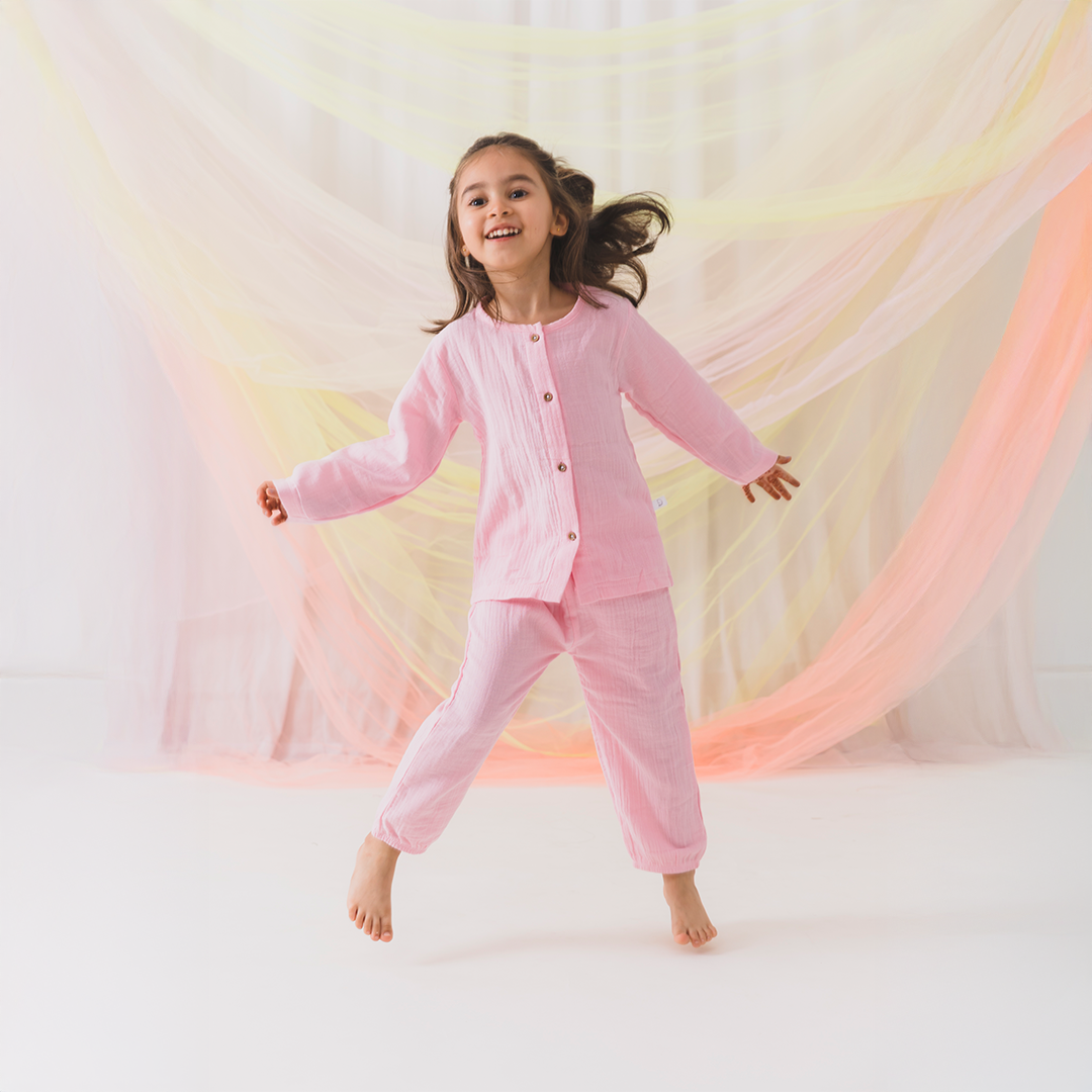 Child in pink pajamas standing against a soft, multicolored background