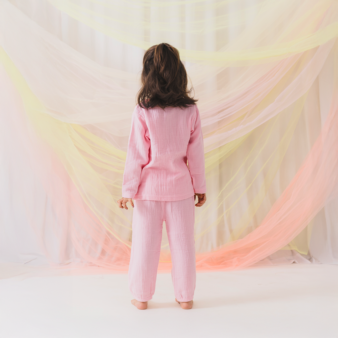 Person wearing a pink outfit standing in front of colorful fabric