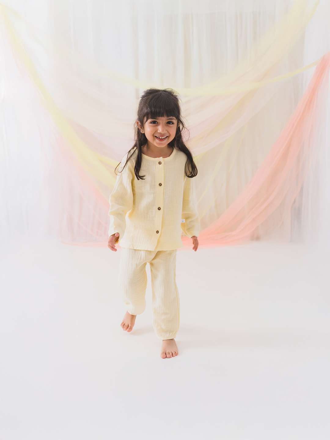 Child wearing a cream-colored outfit standing in front of colorful fabric drapes.