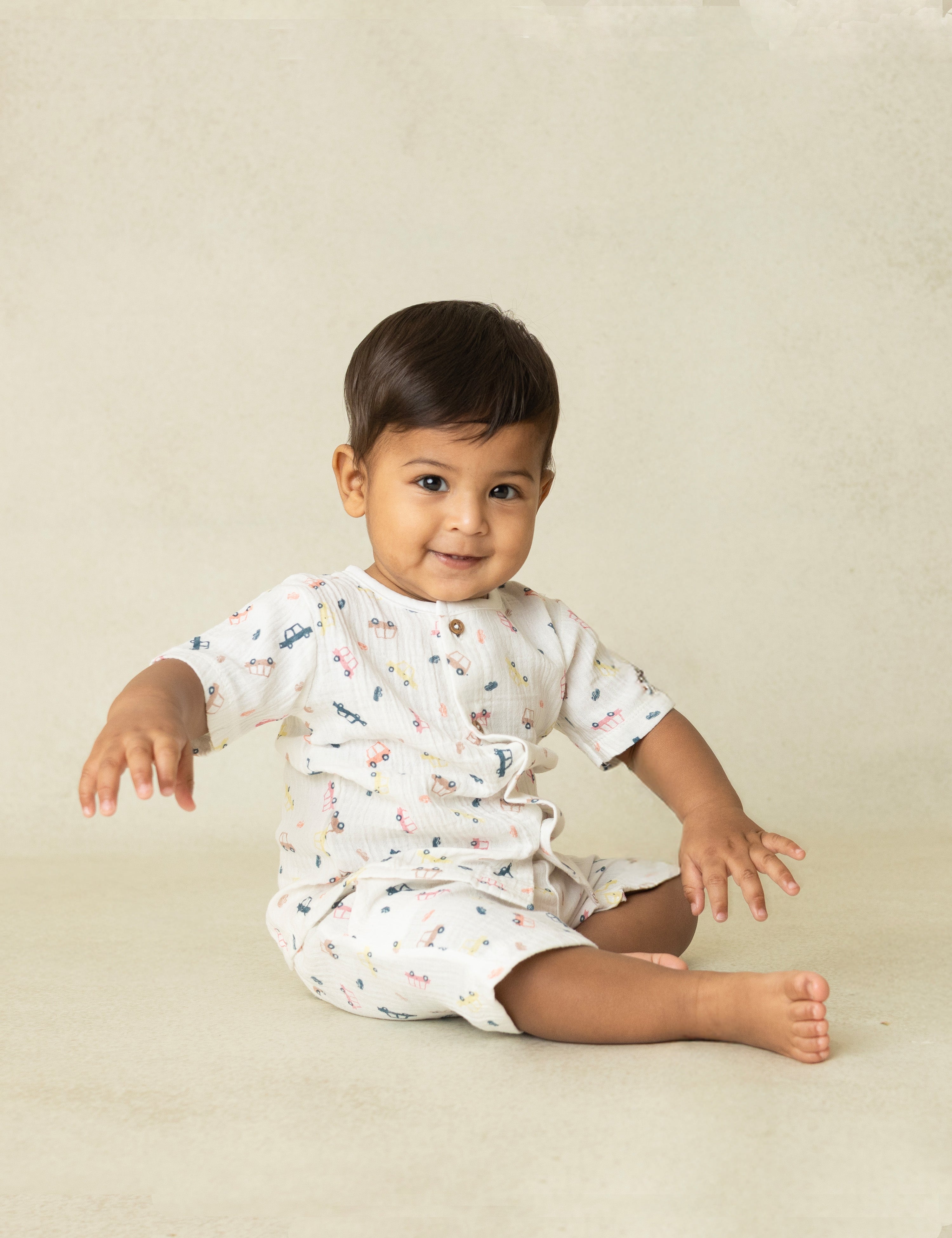 Baby sitting on a beige surface wearing a white outfit with colorful patterns.