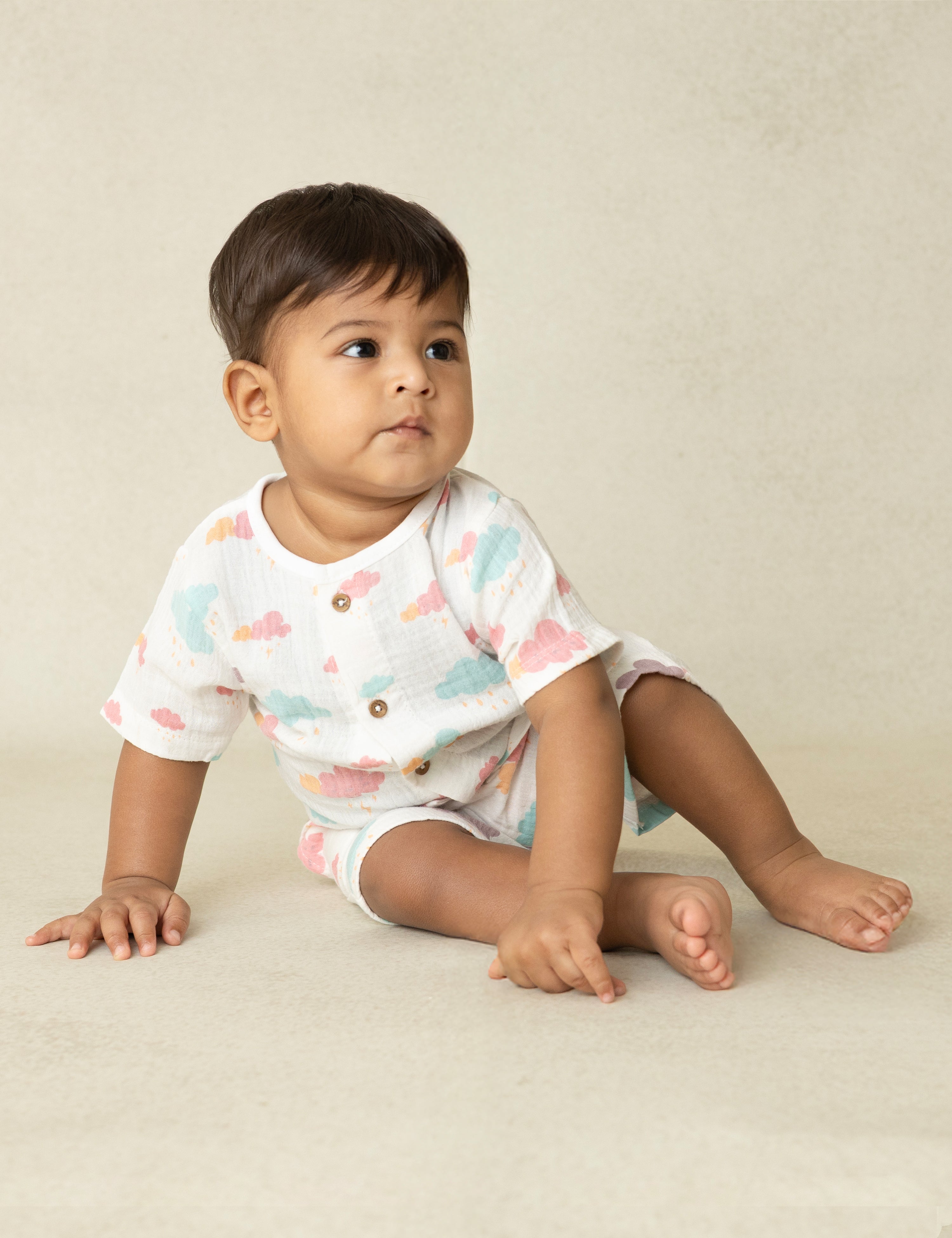 Baby sitting on a beige surface wearing a white onesie with colorful butterfly pattern.