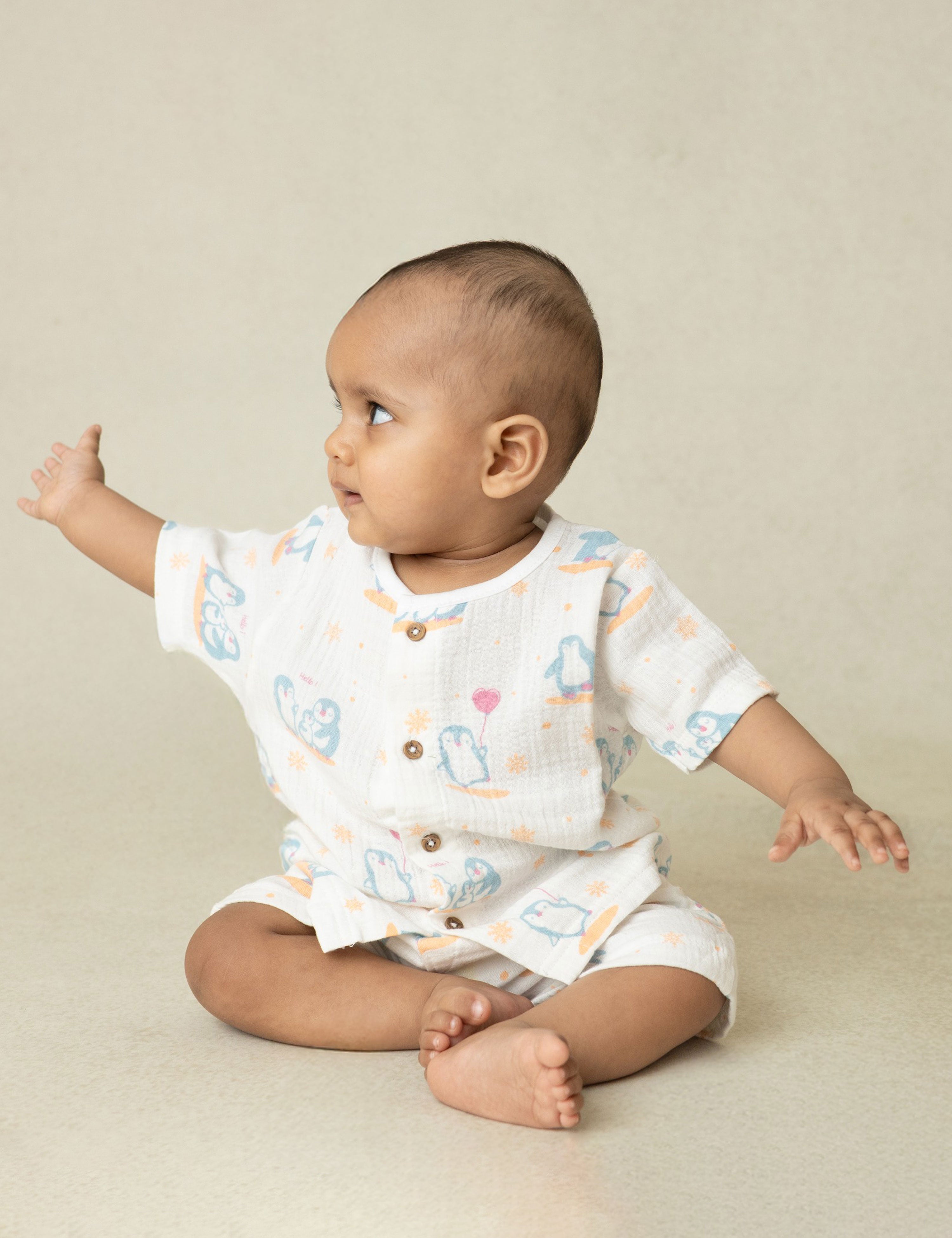 Baby wearing a white outfit with colorful patterns on a beige background