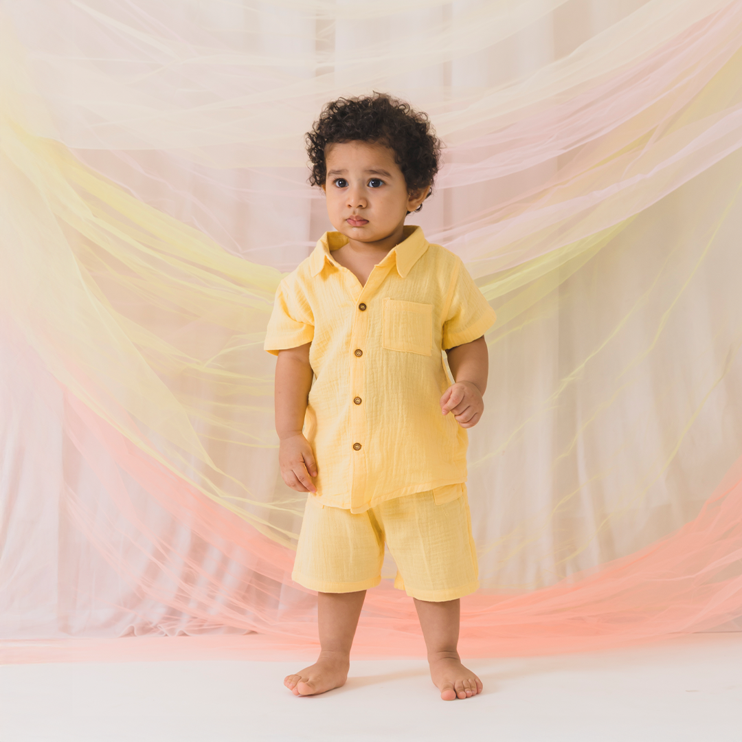 Child wearing a yellow outfit standing in front of a soft, multicolored backdrop